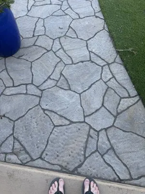 Stone pathway with irregular stone patterns beside a patch of grass and a blue pot, with feet visible at the bottom.
