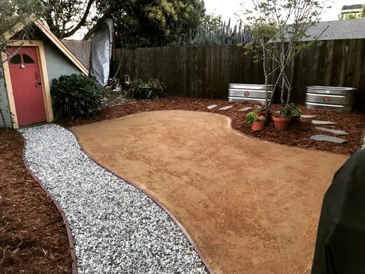 A landscaped garden featuring a gravel path, potted plants, and a small shed, designed by Quilici Gardening in Santa Cruz.