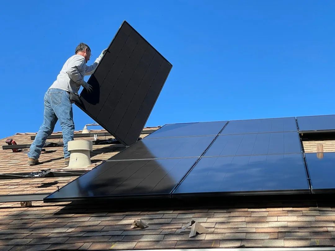 A worker installs solar panels on a roof under a clear blue sky, representing ROOFMASTERS' commitment to renewable energy in Suisun City.