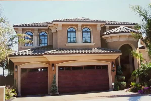 A two-story house with a tiled roof and two wooden garage doors installed by R & P Garage Doors in Byron.