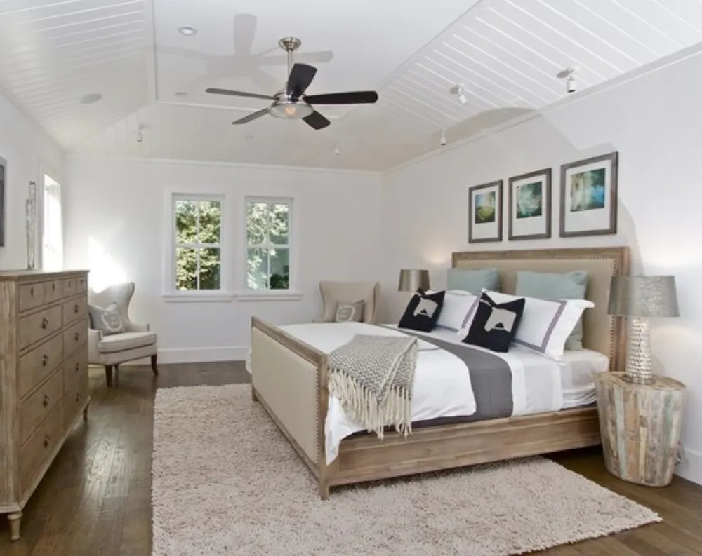 A modern bedroom with wooden flooring, a large bed with neutral bedding, a soft area rug, two side tables, and a dresser, showcasing flooring from Rafael Floors, Abbey Carpet Center in San Rafael.