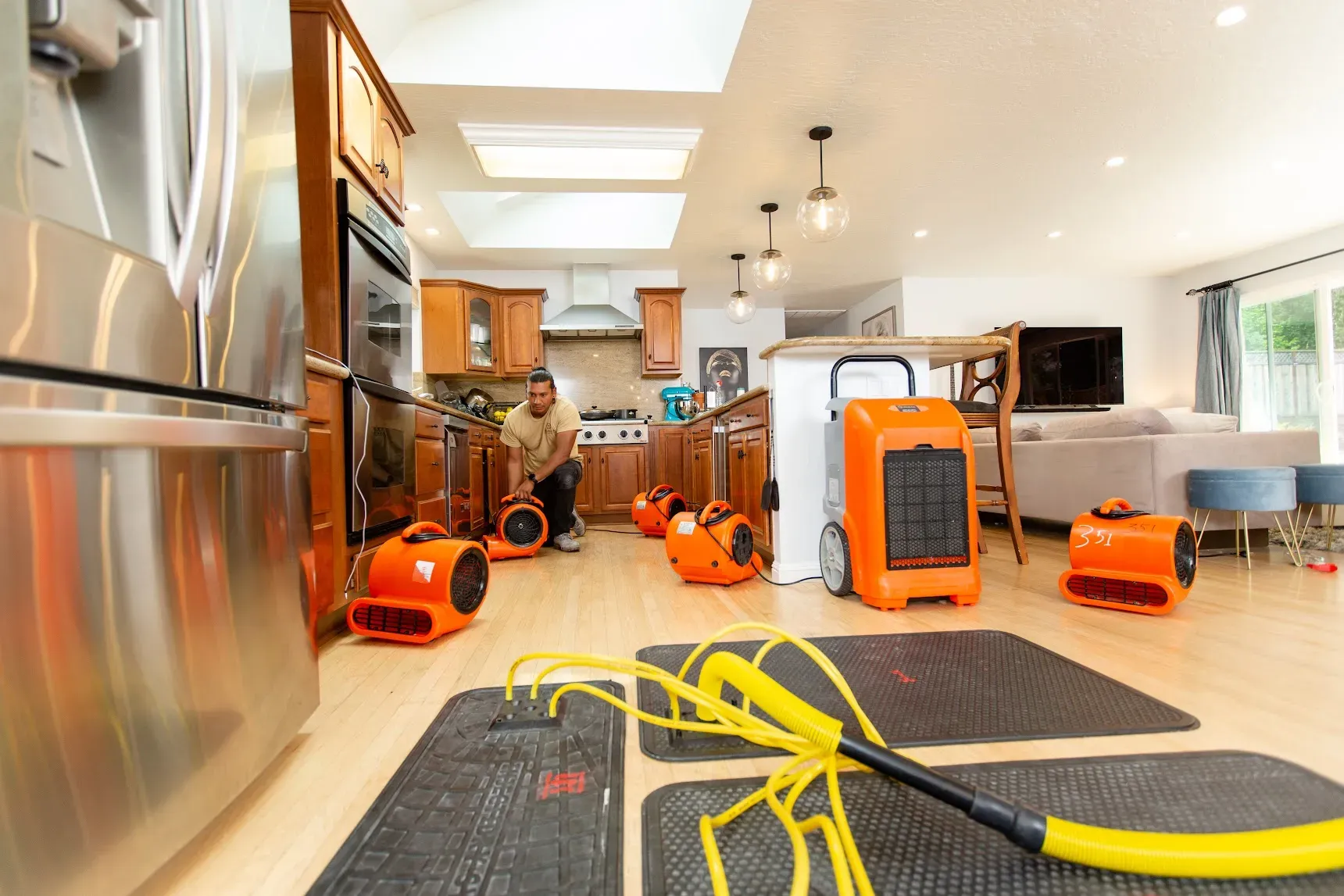 A person setting up orange drying equipment on a kitchen floor, with more equipment scattered around, in a modern kitchen setting.