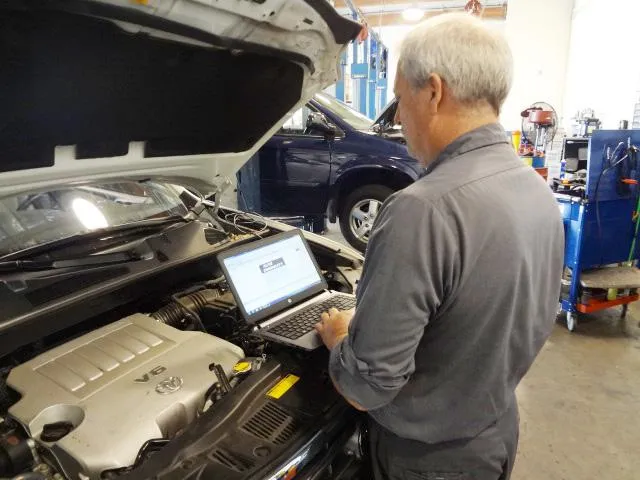 A mechanic at Renson Automotive in Campbell using a laptop to diagnose a car issue in the garage.
