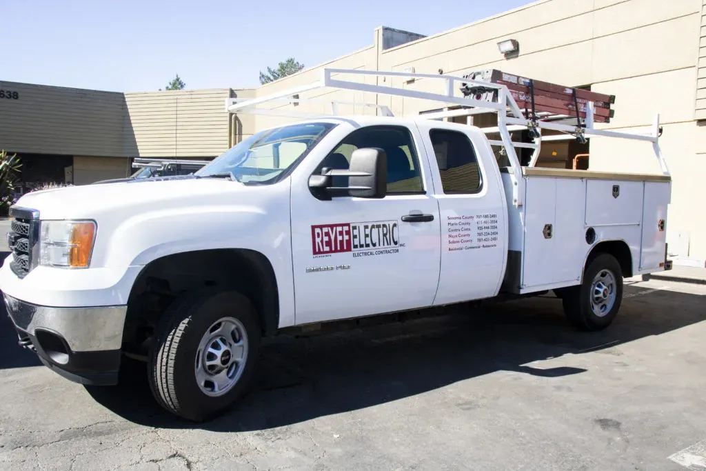 A white service truck belonging to Reyff Electric, Inc. in Rohnert Park, equipped with a ladder and utility compartments, parked in an industrial area.
