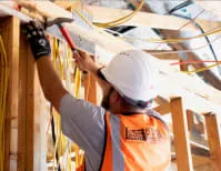 A worker from Reyff Electric, Inc. in Rohnert Park, wearing a hard hat and safety vest, installs electrical wiring on a construction site.