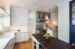 A modern kitchen with white cabinets, a stainless steel range, and a wooden island centerpiece, showcasing the lighting work of Roberts Electric Company, Inc. in Oakland.