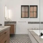 A modern bathroom featuring sleek lighting, a wooden vanity, a built-in bathtub, and patterned floor tiles, designed by Roberts Electric Company, Inc. in Oakland.