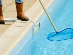 A person using a pool net to clean a swimming pool, representing Roger's Pool & Spa Service Inc. in Sebastopol.