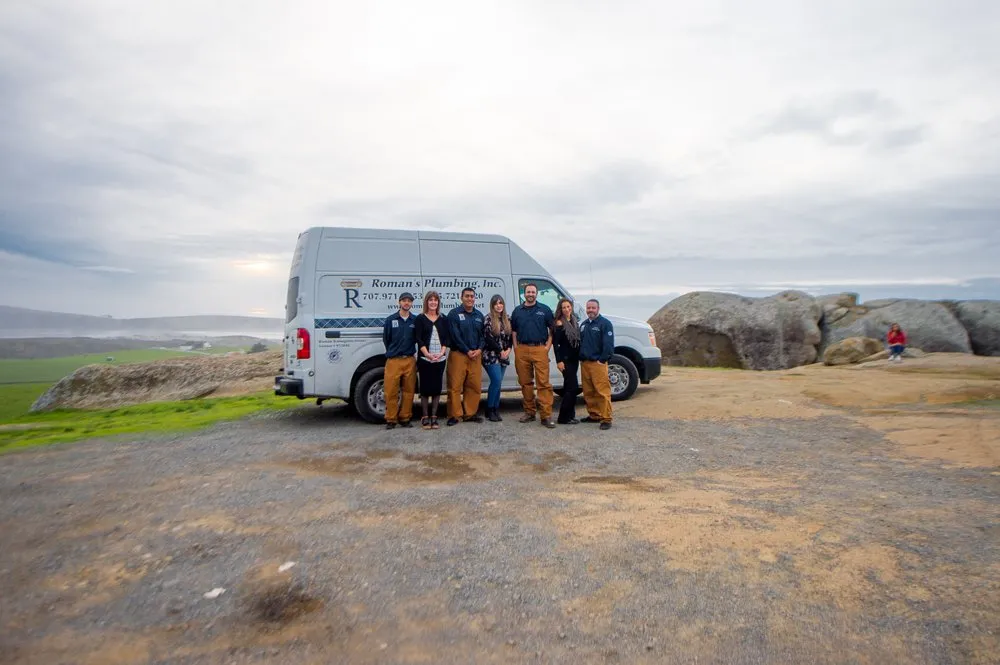 Group of people standing together in front of a Roman's Plumbing, Inc. van with a scenic backdrop, showcasing a dedicated plumbing team in Petaluma.