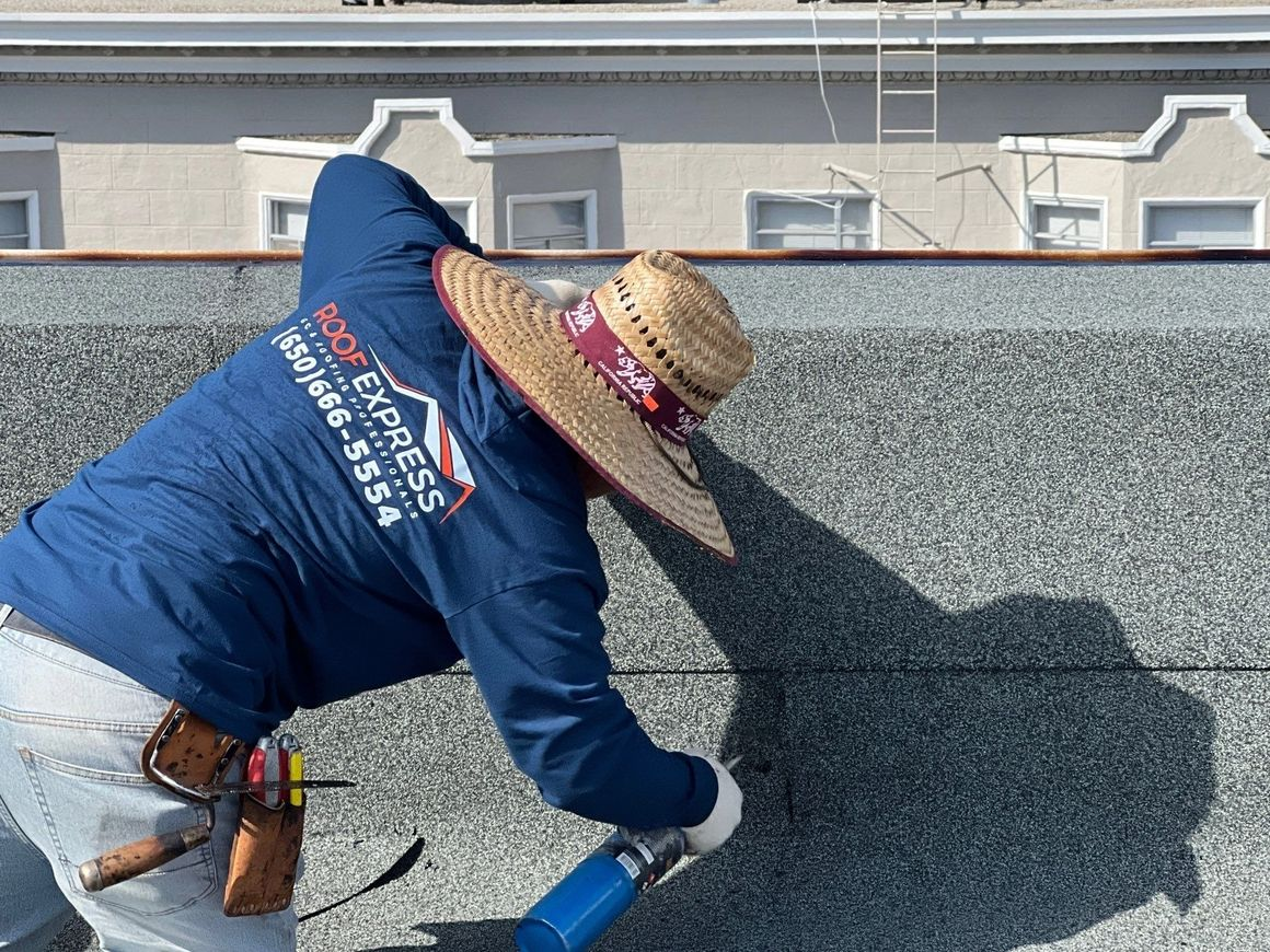 "A professional from Roof Express working on a roof in San Francisco, wearing a branded shirt and holding a tool."