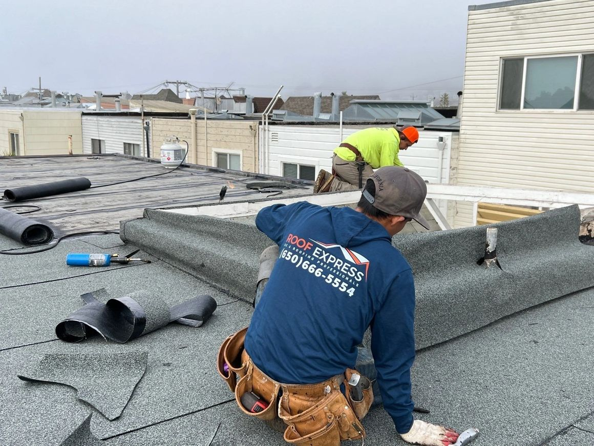 Two workers from Roof Express installing roofing materials on a building in San Francisco, with tools and equipment visible.