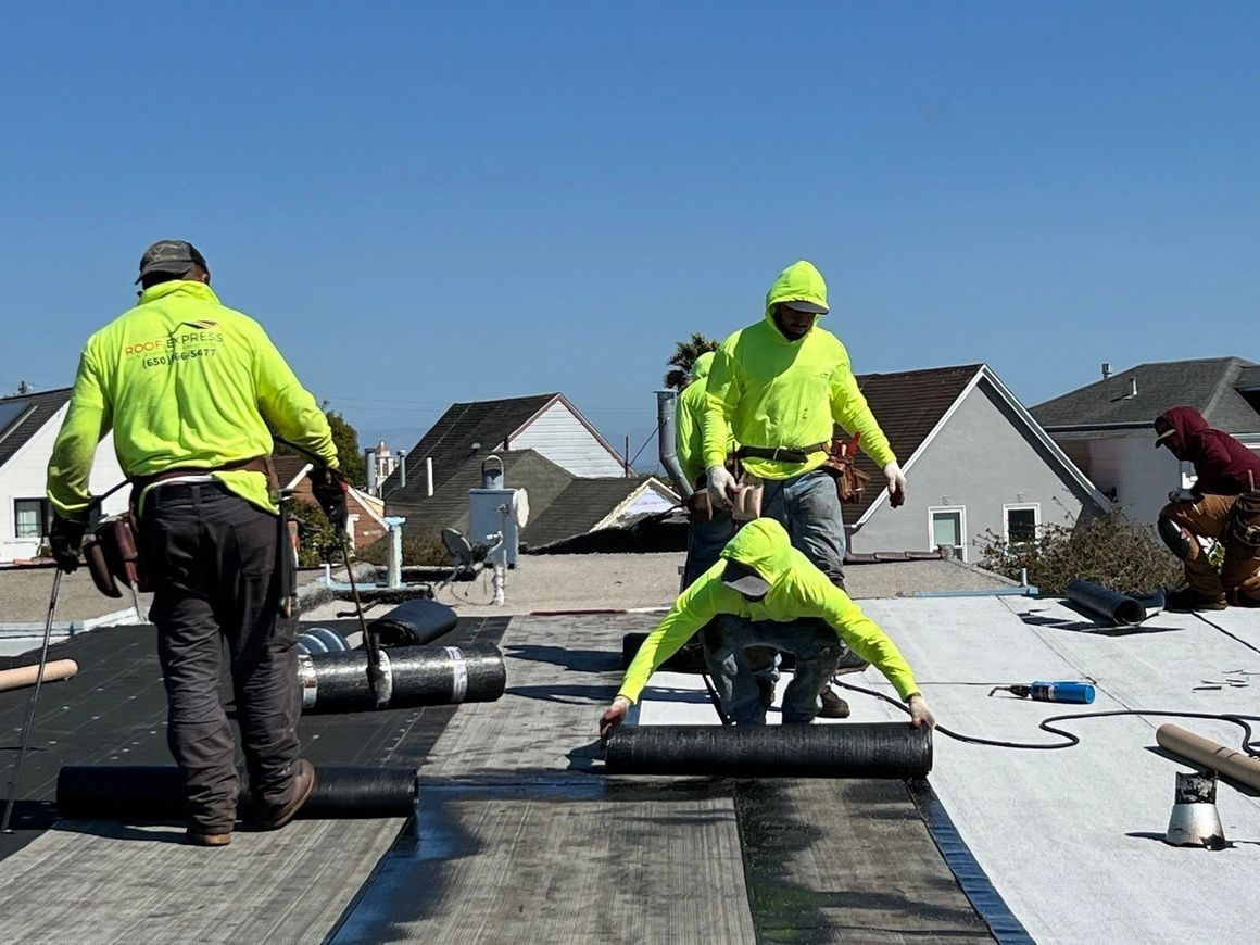 Workers from Roof Express in San Francisco installing roofing materials on a residential roof under clear blue skies.