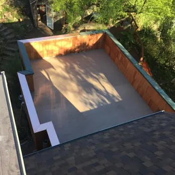 "A rooftop view showcasing a flat roof installation by Roofing Logistics, Inc. in Oakland, surrounded by greenery."