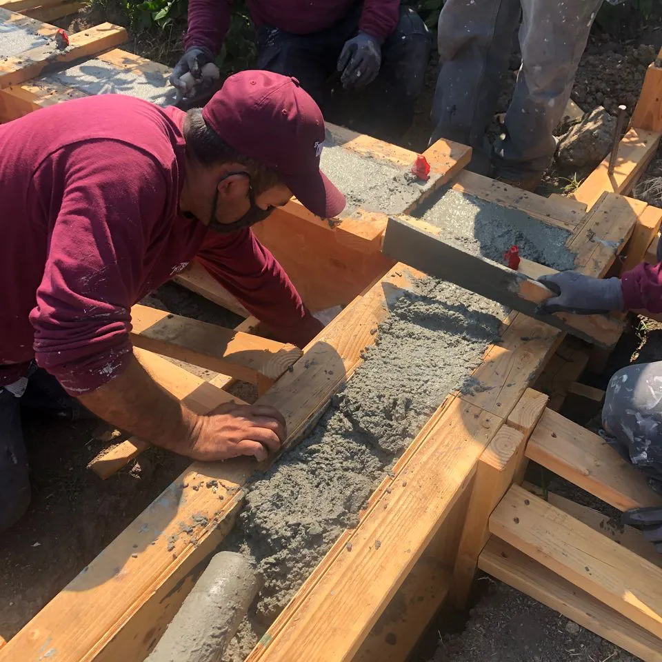 Workers from SF Craftsman, Inc. in San Francisco meticulously smoothing concrete on a wooden frame at a construction site.