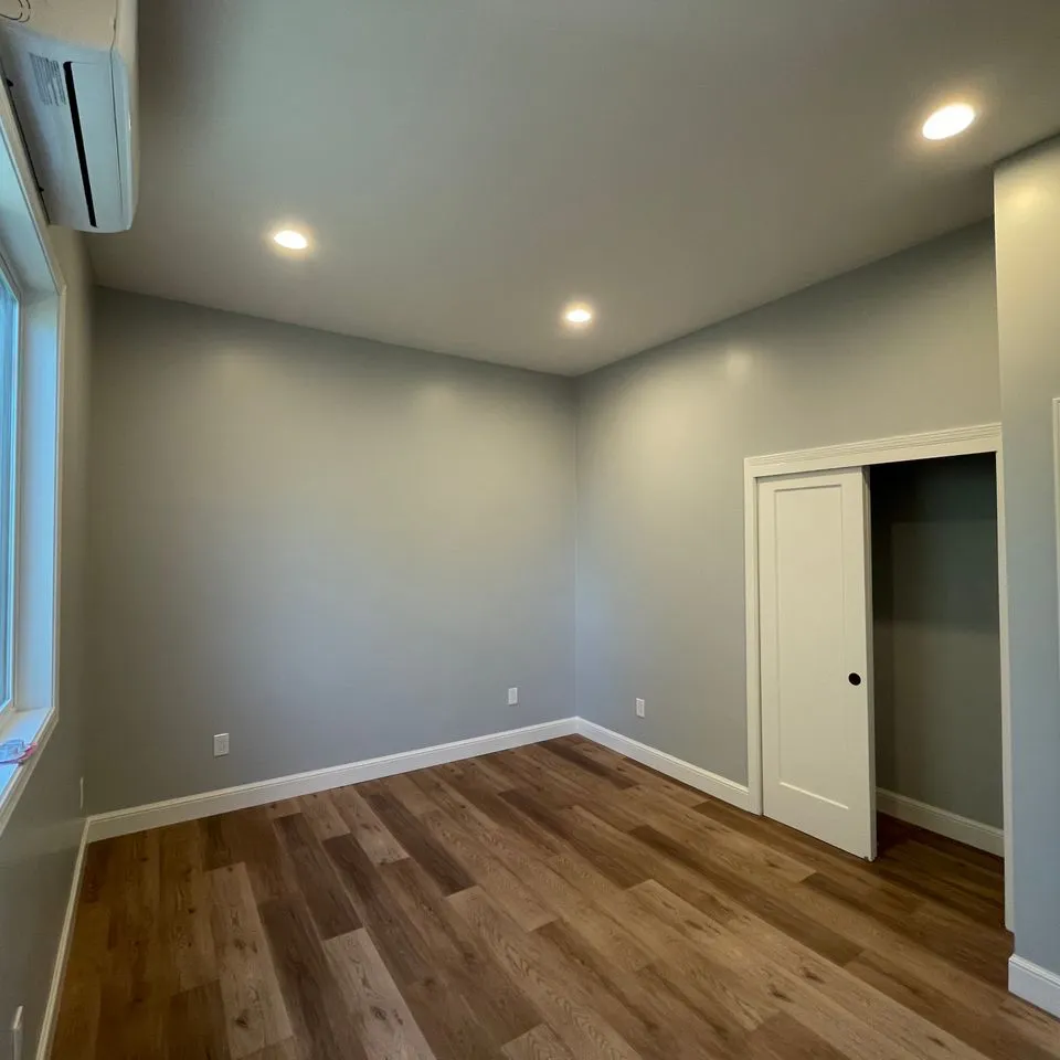 A small, empty room with light gray walls, wooden flooring, ceiling lights, and a sliding closet door, designed by SF Craftsman, Inc. in San Francisco.