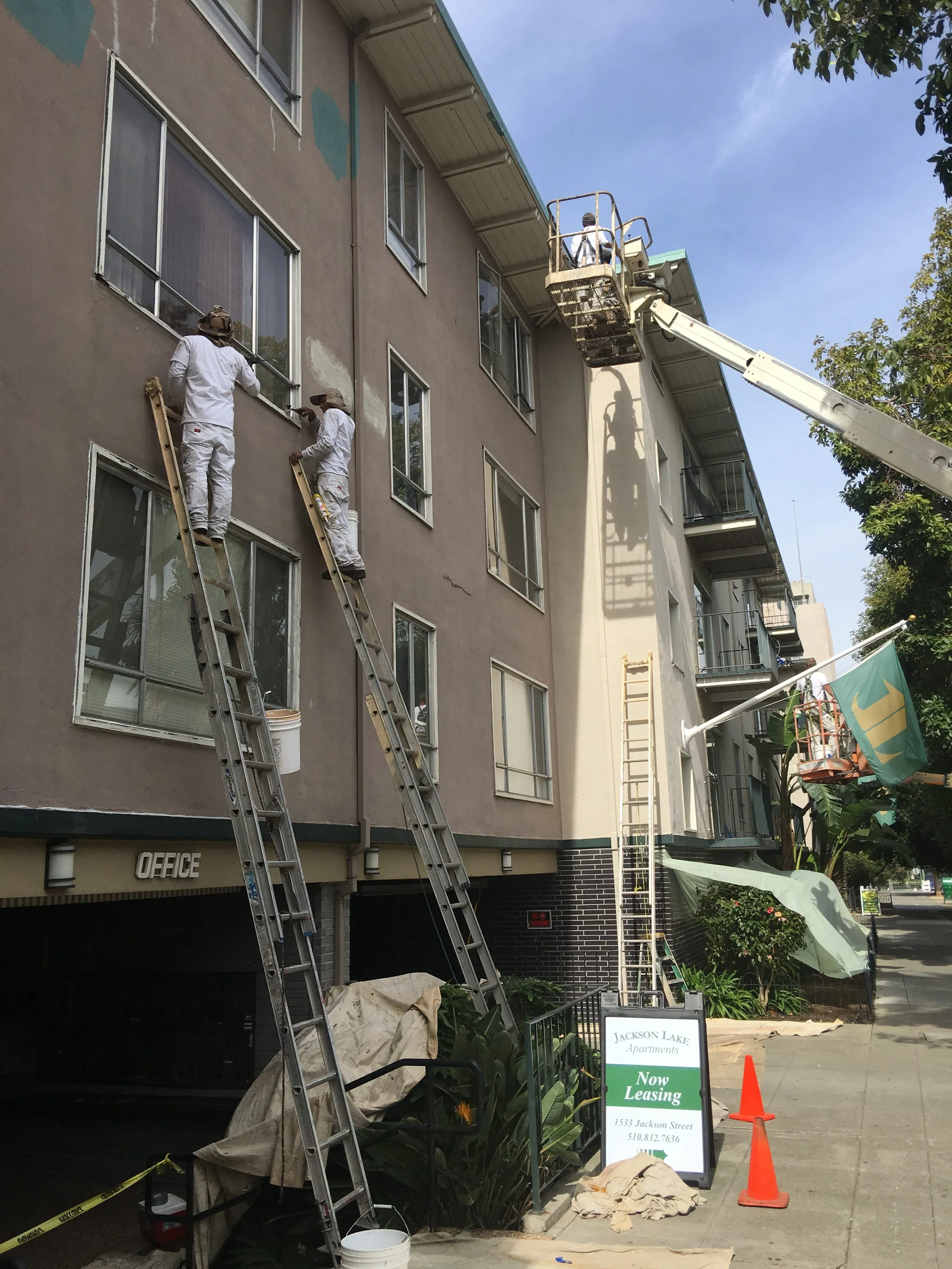 Workers from S & S Painting and Coatings, Inc. on ladders and a lift, painting the exterior of a multi-story apartment building in Castro Valley.