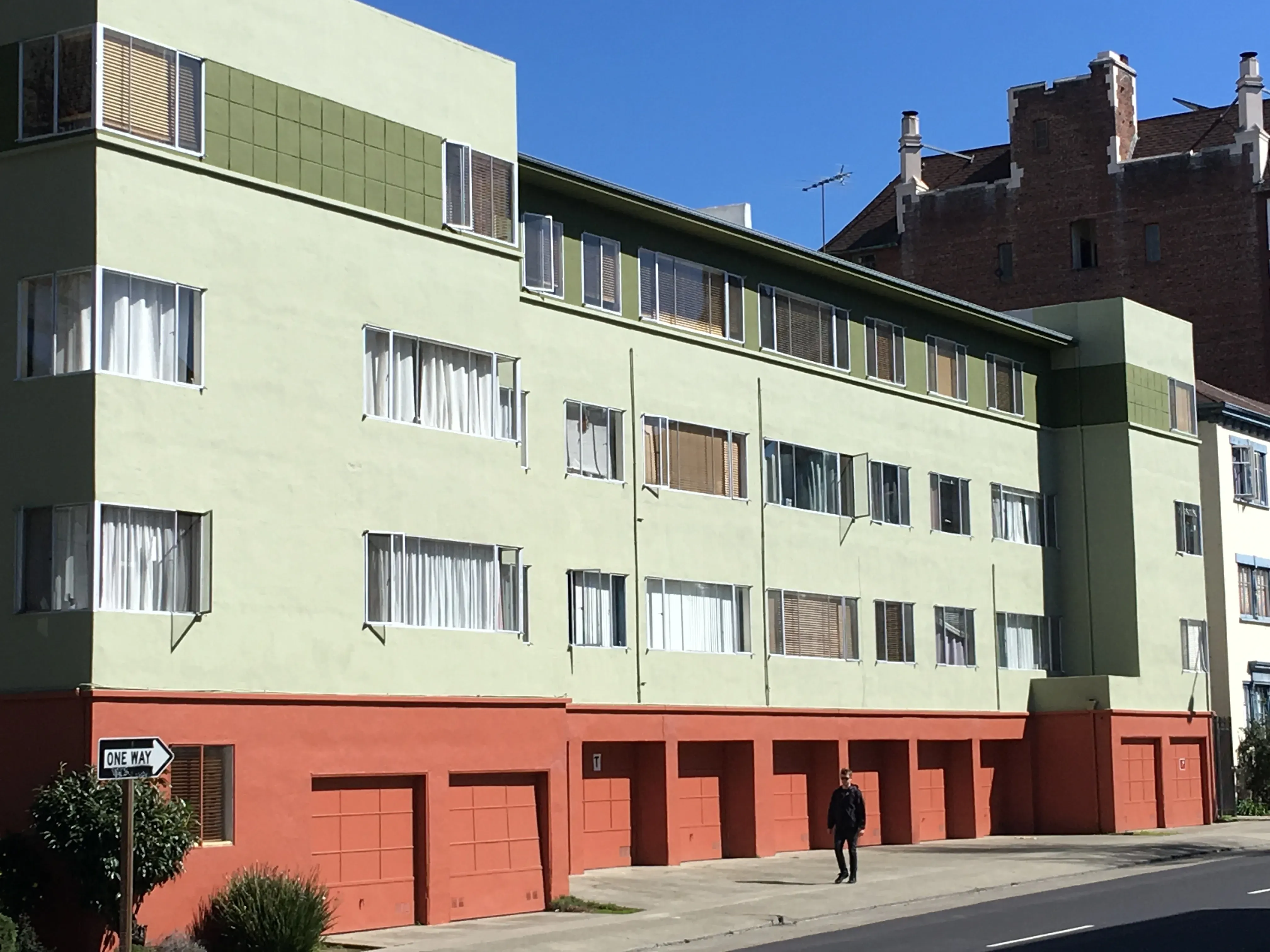 A multi-story building in Castro Valley with a fresh facade, featuring light green walls and orange garage doors, showcasing the work of S & S Painting and Coatings, Inc.