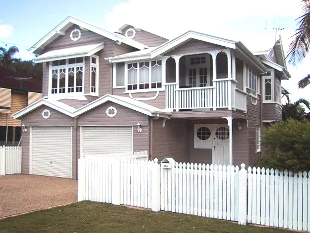 A two-story house with gray exterior walls and white trim, featuring a white picket fence and two garage doors.