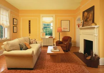 A warmly painted living room in shades of yellow with a cream sofa, wooden coffee table, and a decorative white fireplace, demonstrating the work of S & S Painting and Coatings, Inc. in Castro Valley.