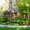 A beautifully landscaped garden featuring lush greenery and a charming brown house in the background, created by Sampson's Landscaping, Inc. in Novato.
