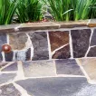 Close-up of a well-constructed stone wall and paved surface with greenery in the background, created by Sampson's Landscaping, Inc. in Novato.