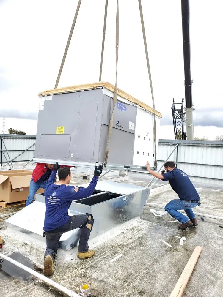 Technicians from SanJoseHeating&Cooling installing a large HVAC unit on a rooftop in SanJose using a crane.
