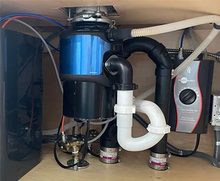 A neatly organized under-sink plumbing installation featuring various pipes and a garbage disposal unit, showcasing the quality work of San Jose Plumbing, Inc. in San Jose.