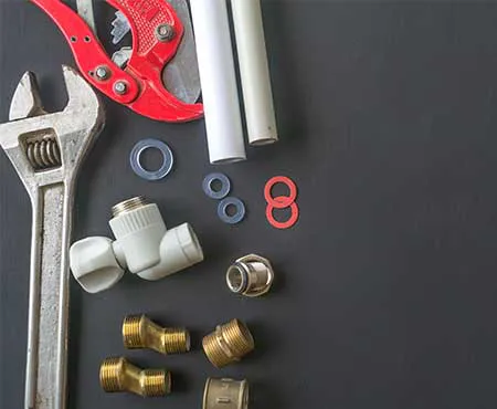 A collection of plumbing tools and fittings, including a wrench, pipe cutter, and various pipe connectors, displayed on a dark surface.