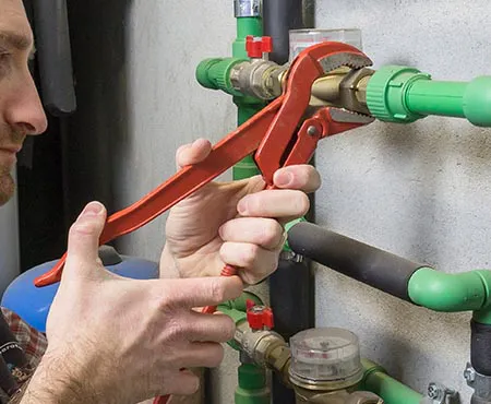 A person using a wrench to tighten green plumbing pipes, showcasing the expertise of San Jose Plumbing, Inc.
