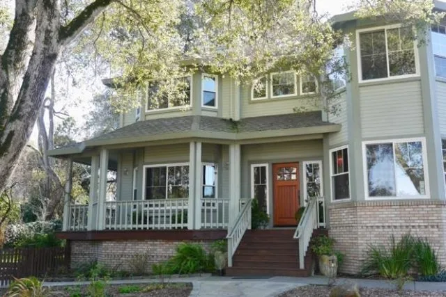 A charming two-story house with a wraparound porch, surrounded by trees, showcasing the work of Save Energy Company in Petaluma.