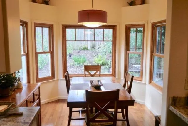 A bright dining area in Petaluma with large windows offering natural light, complemented by a wooden table and chairs, showcasing energy-efficient installations by Save Energy Company.