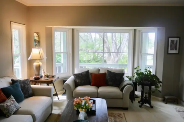 A cozy living room with sofas, a coffee table, and large windows overlooking greenery, showcasing energy-efficient home features.