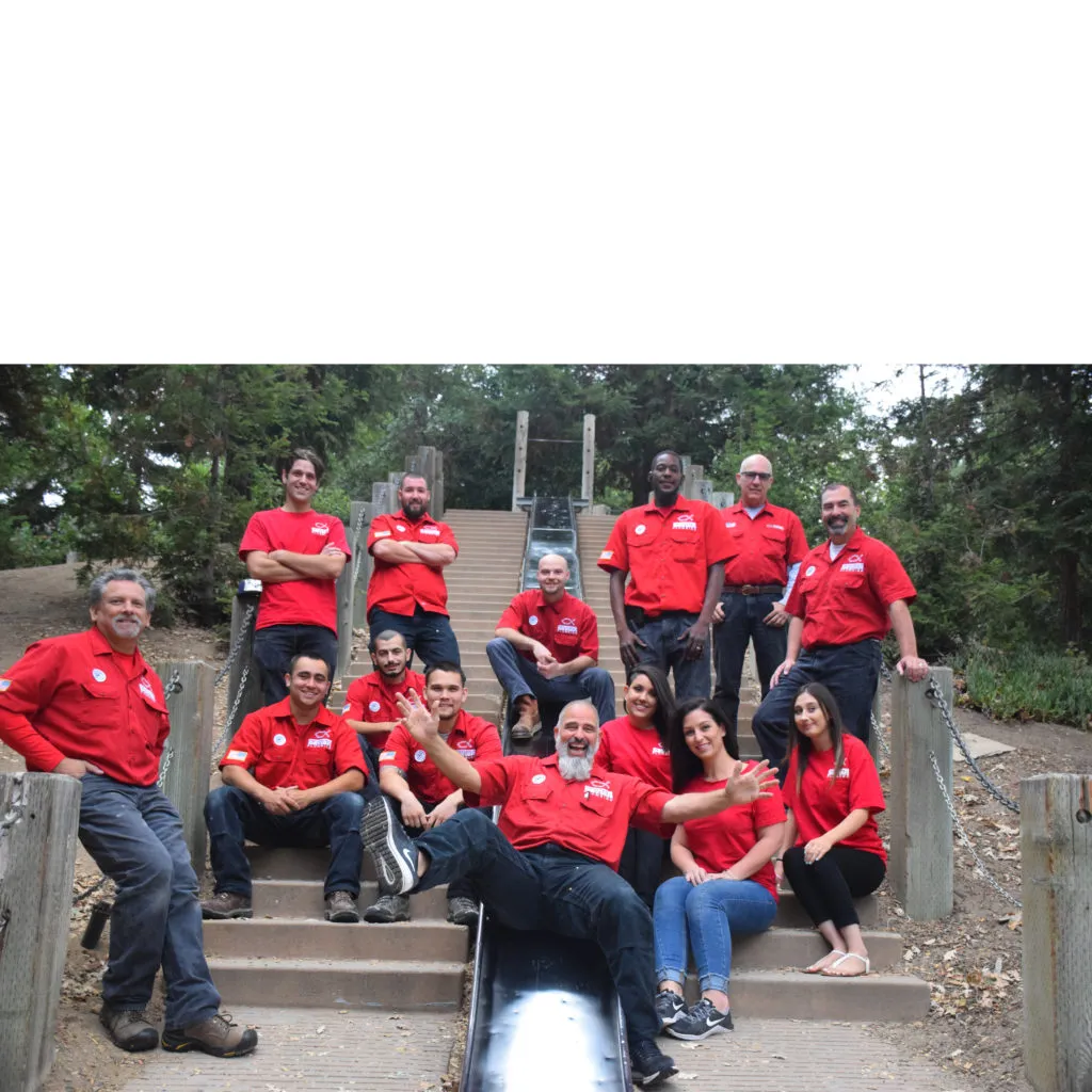 "A group photo of the Savior Plumbing, Inc. team in Pleasanton, wearing red shirts and posing together on outdoor steps with a wooden railing and trees in the background."