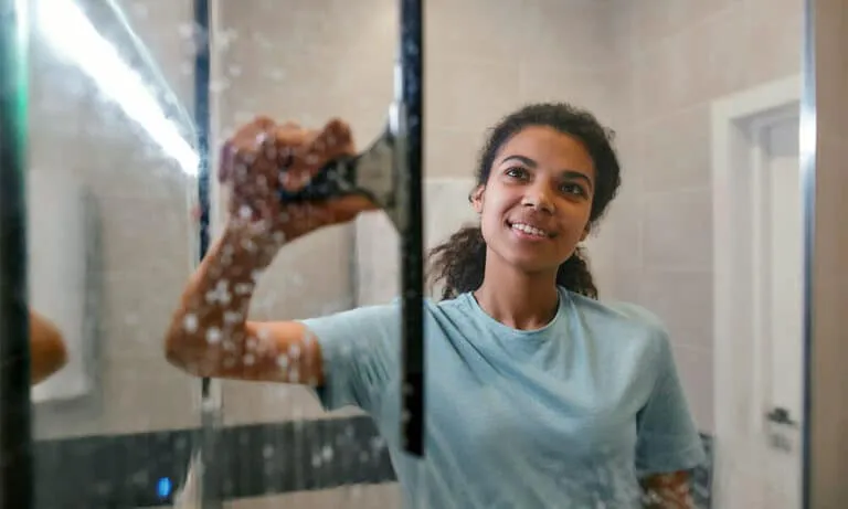 "Person cleaning a glass shower door, showcasing the quality and clarity of Schicker Luxury Shower Doors, Inc. in Concord."