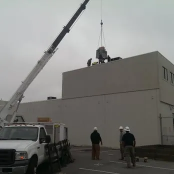 A crane lifting HVAC equipment onto the roof of a commercial building with workers and Schmitt Heating Company, Inc. staff in San Francisco.