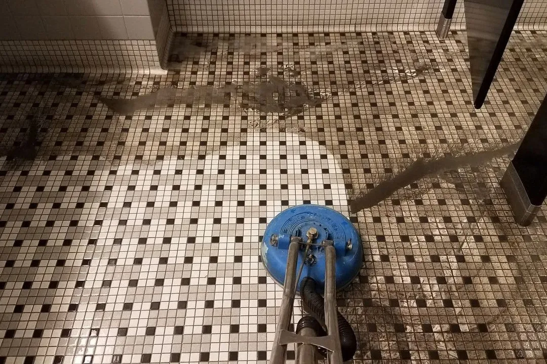 A tile floor showing a sharp contrast between the dirty area and the cleaned section, with a steam cleaning machine in process.