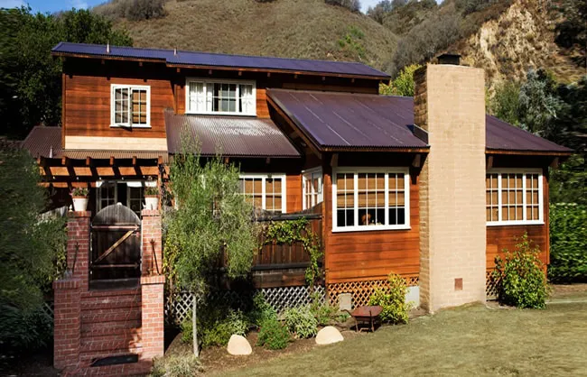 A rustic house with wooden siding and a metal roof, bordered by greenery, representing the work of Scudder Roofing Company in Monterey.
