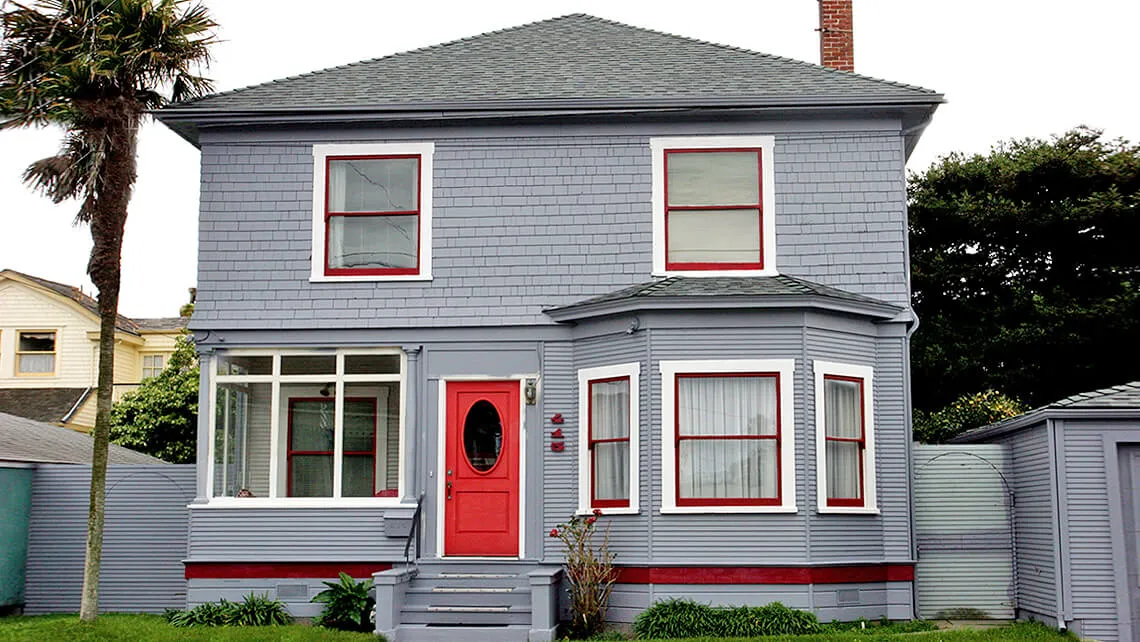 "A well-maintained two-story house with grey siding and red accents, showcasing Scudder Roofing Company's work in Monterey."