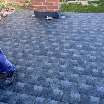 "A close-up view of a newly shingled roof with a worker's foot partially visible and a brick chimney in Sunnyvale, completed by Sersiv Roofing Corporation."