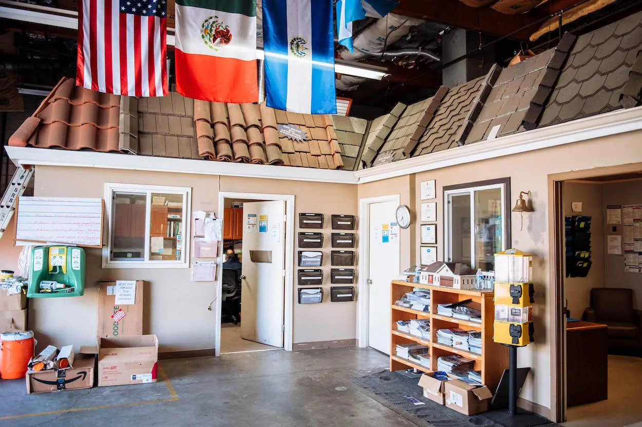 An interior view of Sierra Roofing & Solar in Dublin, featuring a display of various roofing materials and international flags hanging from the ceiling in a well-organized workspace.
