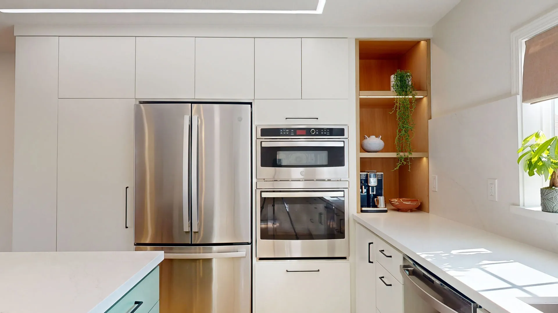 A modern kitchen featuring sleek white cabinetry, a stainless steel refrigerator, built-in oven, and open shelving with decorative items, designed by Sigura Construction, Inc. in San Jose.