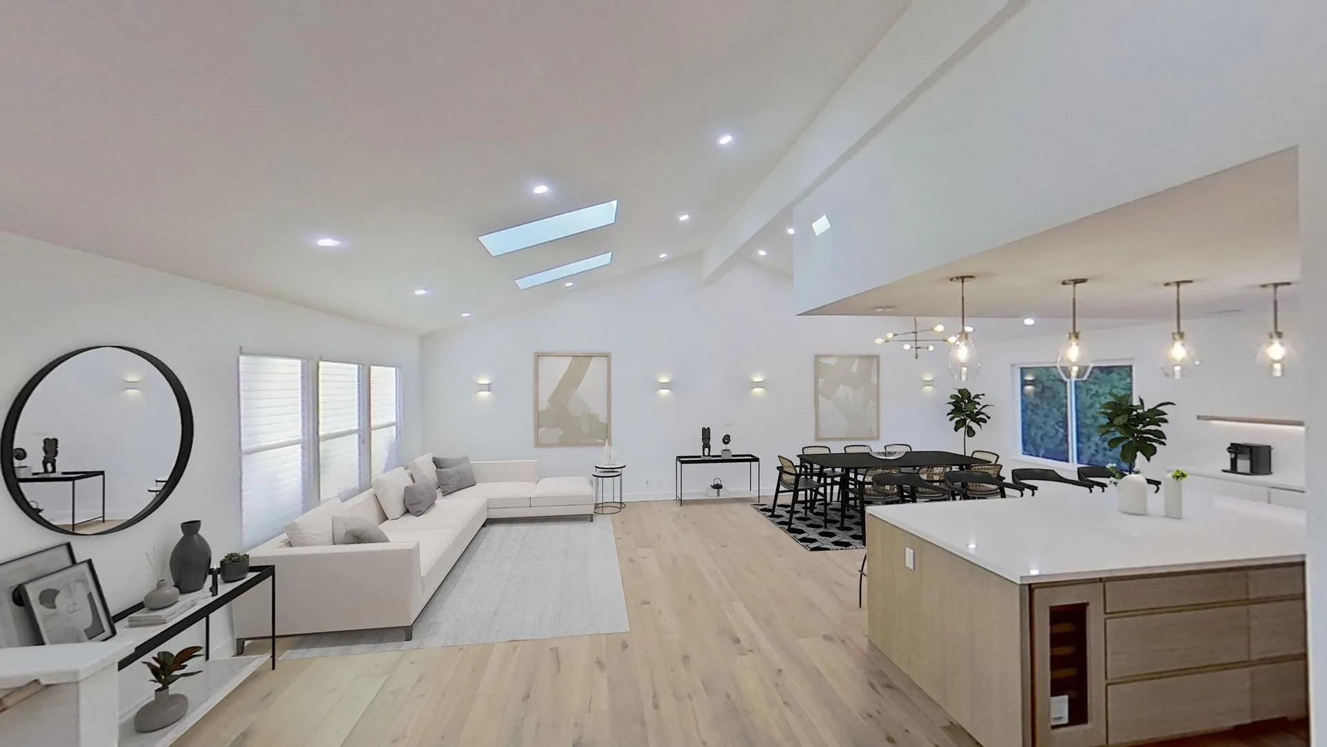 A modern open-concept living room and kitchen in San Jose, featuring a sleek design with a large sofa, dining area, skylights, and pendant lights by Sigura Construction, Inc.