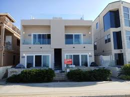 A modern two-story house with a beige exterior and large windows, showcasing a recent paint job by Sigura Pro Painting in San Jose.