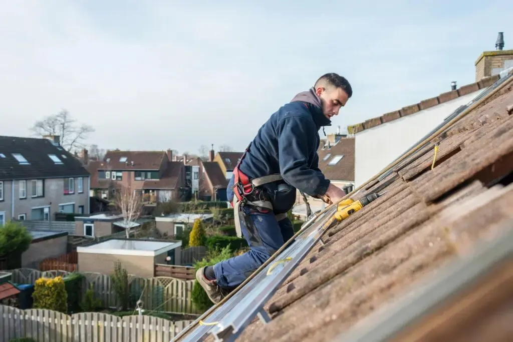A worker from Simon Says Roofing in San Jose repairing a sloped roof with a drill, surrounded by neighborhood houses.