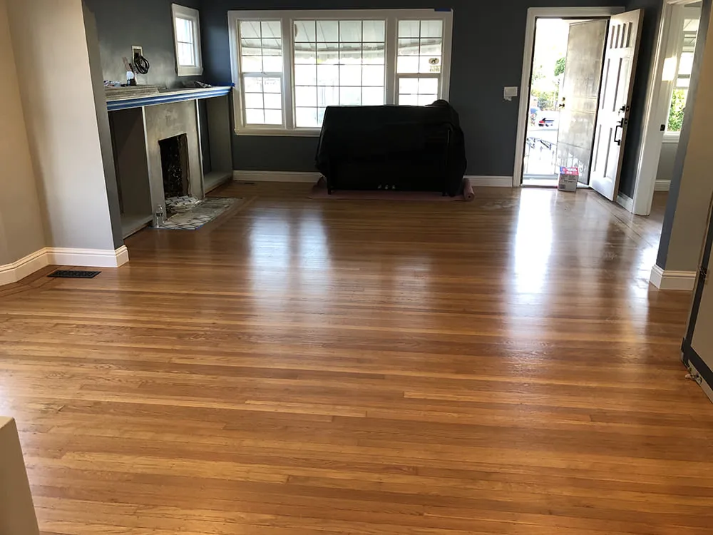 A spacious living room in Winnetka showcasing polished wooden floors, a fireplace, large windows, and an open door, designed by Simple Builders.