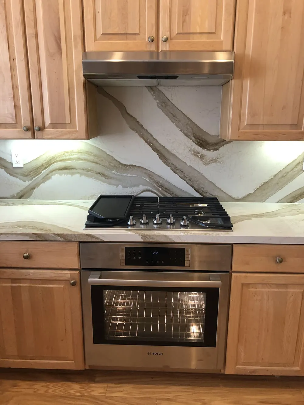 A modern kitchen setup with wooden cabinets, a stainless steel oven, and a sleek, patterned backsplash.