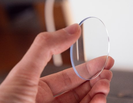 A close-up image of a hand holding a clear eyeglass lens, illustrating a focus on quality optical products at Site for Sore Eyes in Daly City.