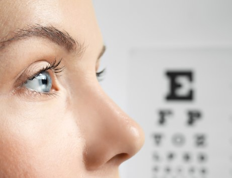 Close-up of a person's eye looking towards an eye chart with blurred letters, representing vision testing at Site for Sore Eyes, Daly City.