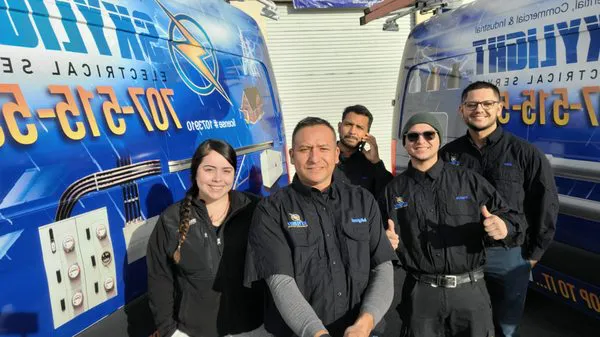 A group of five people in Skylight Electrical Service uniforms standing in front of company vans in Fairfield. They are smiling and showing a thumbs-up gesture, representing their commitment to quality electrical services.
