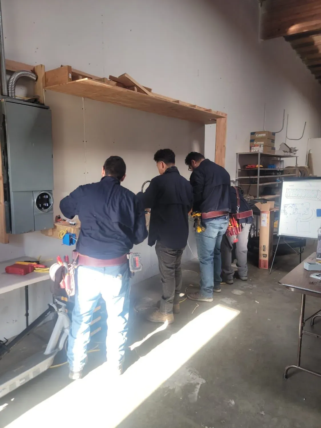 A group of electricians from Skylight Electrical Service working together on electrical installations in a workshop in Fairfield, focusing on tools and equipment.